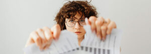 Woman with glasses tearing a paper document by hand, symbolizing the end of inefficient paper-based QMS and the transition to digital document management for ISO 13485 compliance.