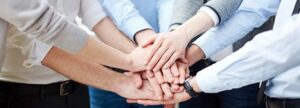A group of office workers and QA/RA professionals joining hands in a team handshake, symbolizing collective cooperation and shared responsibility in a medical device quality management system.